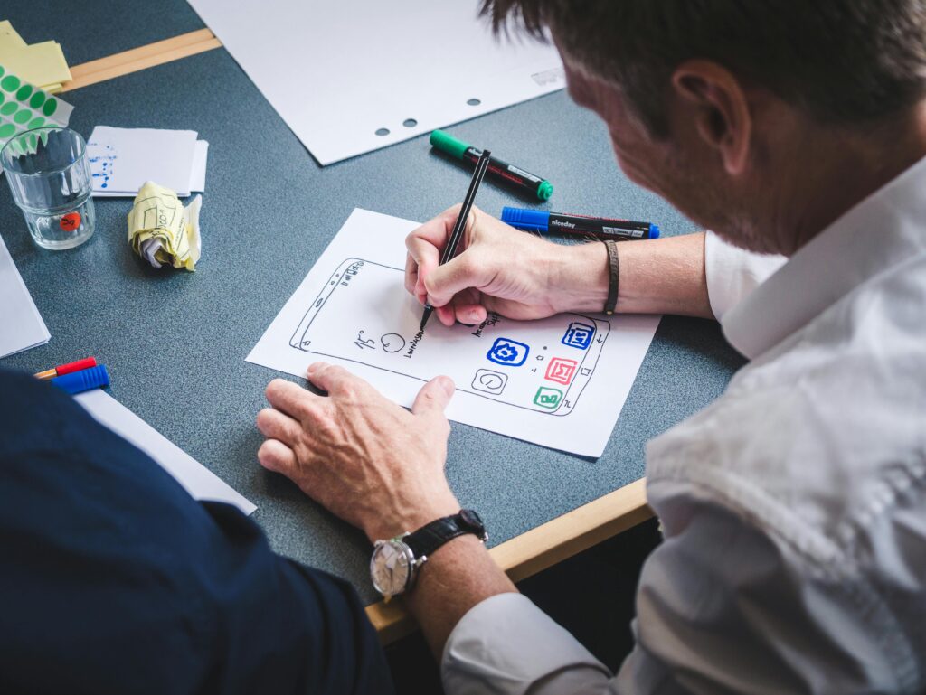 pexels-photo-3471423-3471423 A designer sketches a mobile app prototype on paper at an office desk, focusing on creativity and design.